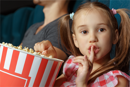 Little girl holding popcorn in a cinema, making a "shh" gesture