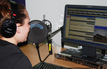 Carmel Sealey sitting at a computer with a microphone recording an audio description track.