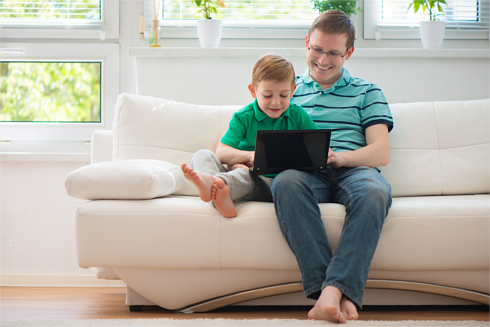 Father and son sitting on a sofa using a laptop together