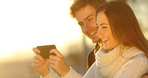 Man and woman smiling while viewing media on a smartphone together