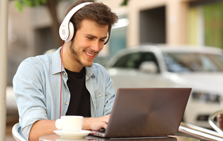 Young man sitting outdoors at a café whilst using a laptop and headphones