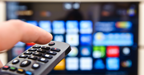 Left hand pointing a remote control at a Smart TV