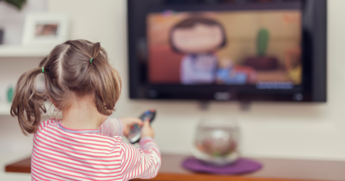 Little girl pointing remote control at a cartoon on TV