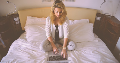Woman sitting on a bed, using a laptop