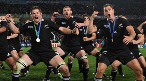 New Zealand rugby team wearing gold medals, performing the haka on the field