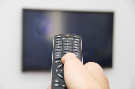 Right hand pointing a remote control towards a TV screen