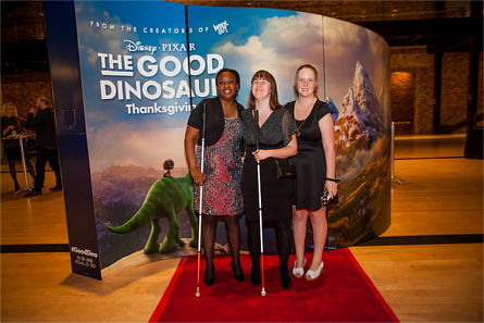 Attendees of Pixar's 'White Canes, Red Carpet' event standing in front of a poster for 'The Good Dinosaur'. Image credit: Guide Dogs for the Blind, Flickr