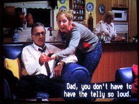 Example of positioned lyrics: Frame from a movie showing a girl saying to her father "Dad, you don't have to have the telly so loud" with positioned captions