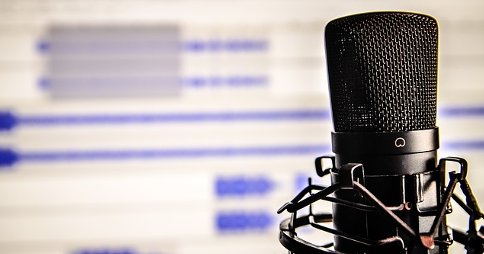 Studio microphone in front of audio waveforms on a screen in the background