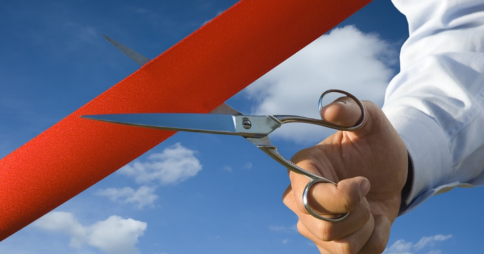 Man's right hand holding open scissors over a line of red tape