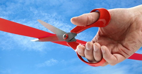 Right hand holding open scissors over a line of red tape