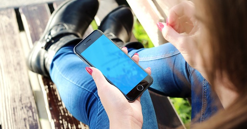 Woman reclining on a wooden park bench outdoors, with an iPhone 6 in left hand