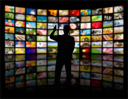 Outline of a man with a remote control in front of a wall of technology screens