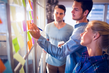 Man writing on Post-it notes with assistance from colleagues