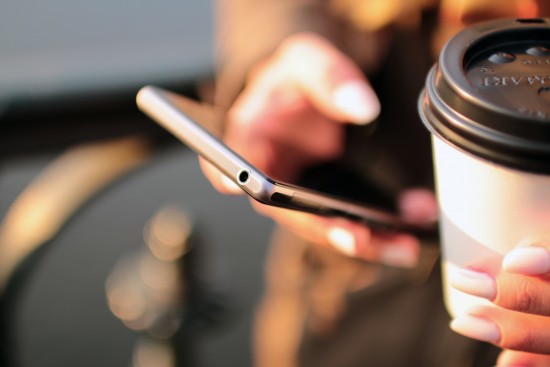 Lady texts with one hand and holds a coffee with the other