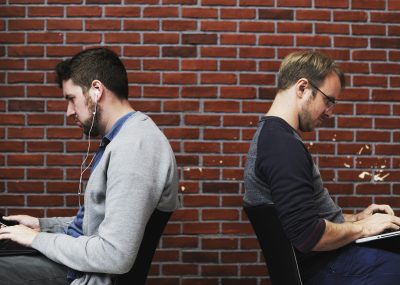 Two men using a phone and a laptop